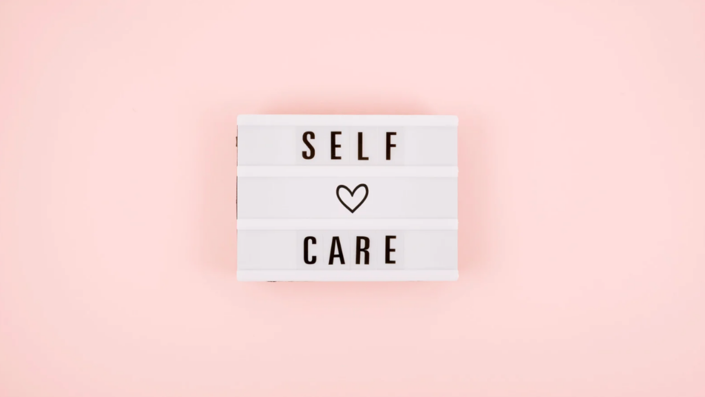 Lightbox sign displaying "SELF CARE" with a heart in the middle on a pastel pink background.