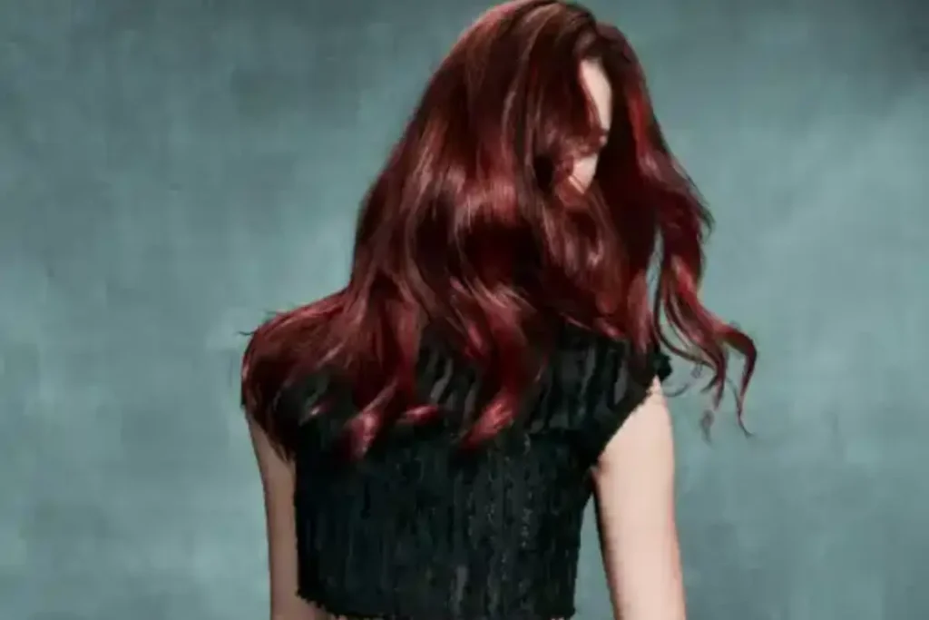 Person with long, wavy dark red hair facing away from the camera, embodying self-care in a sleeveless black top against a plain grey background.